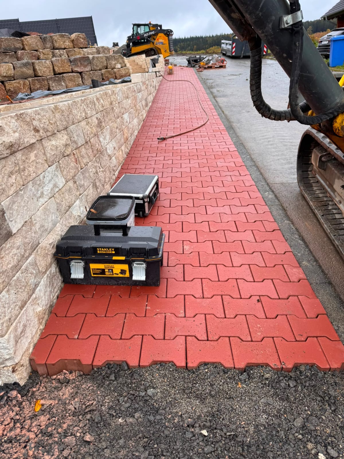 Pflasterweg entlang einer Natursteinmauer mit Bagger im Einsatz